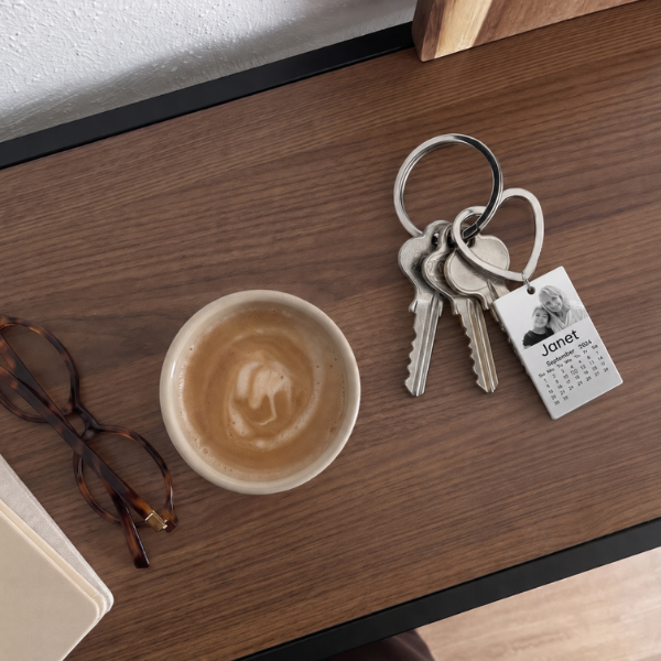 Rechteckiger Kalender-Foto-Schlüsselanhänger auf einem Walnussschreibtisch, Kaffeetasse und Brille daneben